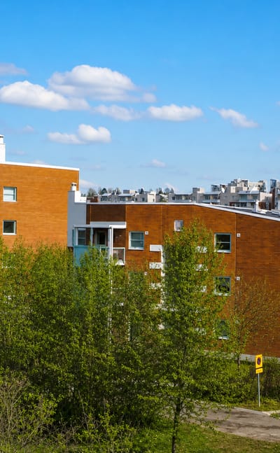 Red-brick and white apartment blocks among green trees under a blue sky in Mellunmäki, eastern Helsinki