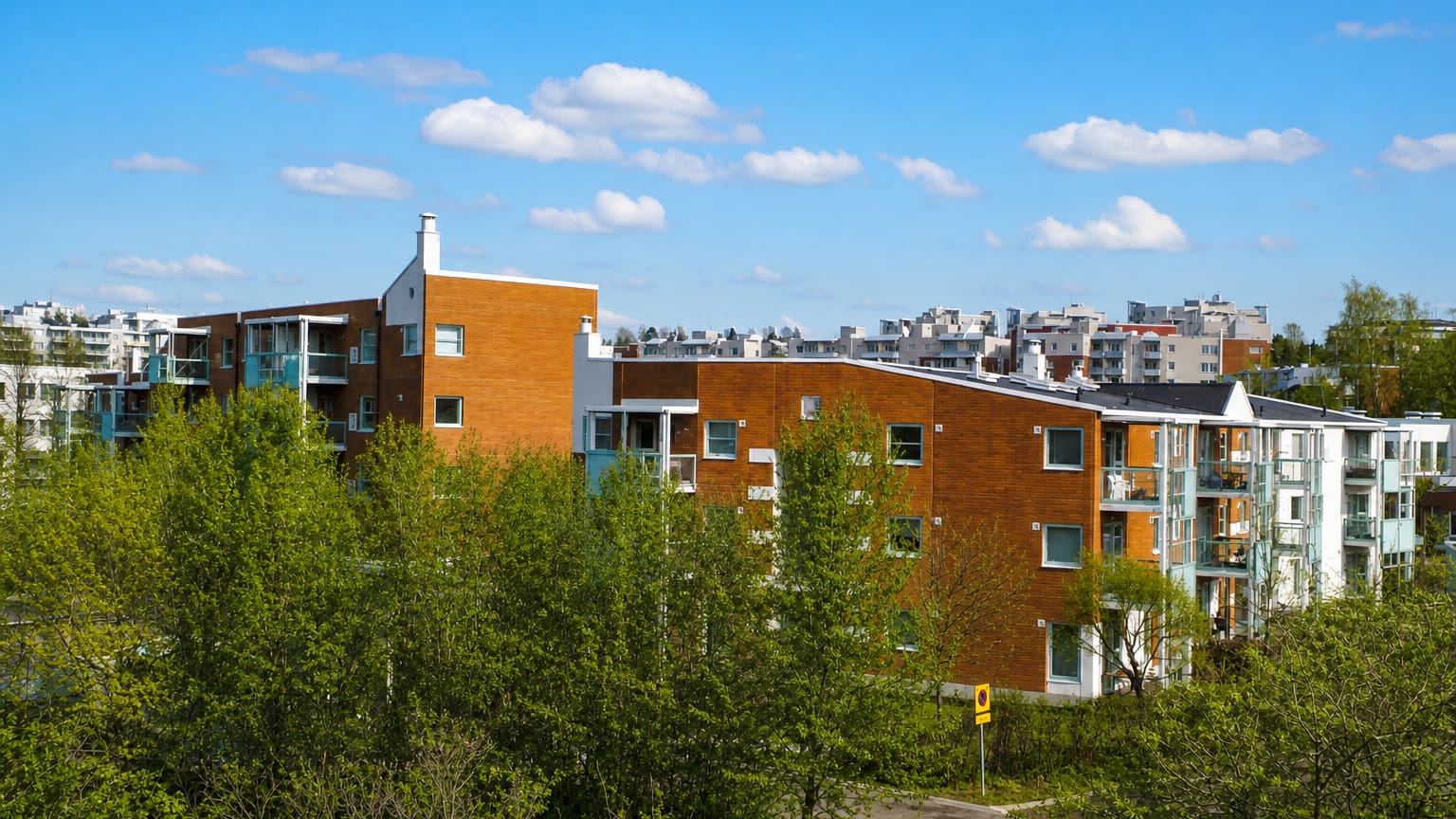 Red-brick and white apartment blocks among green trees under a blue sky in Mellunmäki, eastern Helsinki