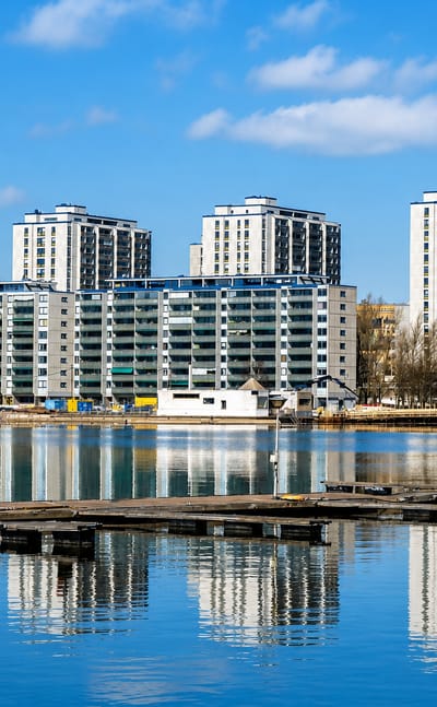Waterfront apartment towers of Merihaka in Helsinki reflected in calm sea water beside floating jetties.
