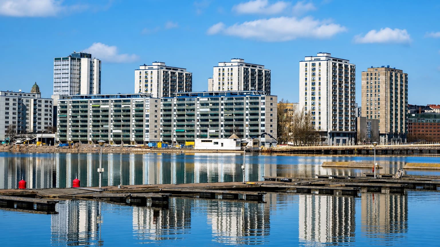 Waterfront apartment towers of Merihaka in Helsinki reflected in calm sea water beside floating jetties.