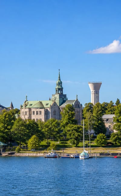 Waterfront townscape of Munkkiniemi, Helsinki, with church spires and a small boat harbour along the shore.