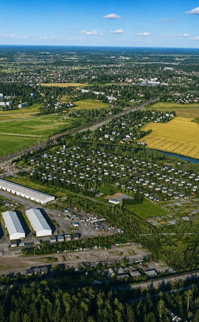 Aerial view of Oulunkylä, Helsinki, with golden summer fields, a winding river, allotment gardens and forest under blue sky