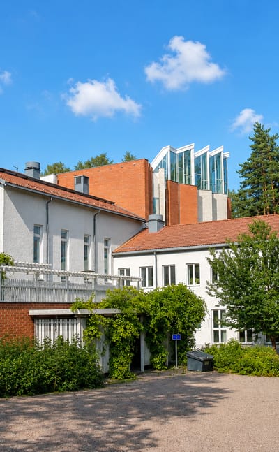 White-rendered and red-brick parish-style building among tall pines in Pakila, Helsinki