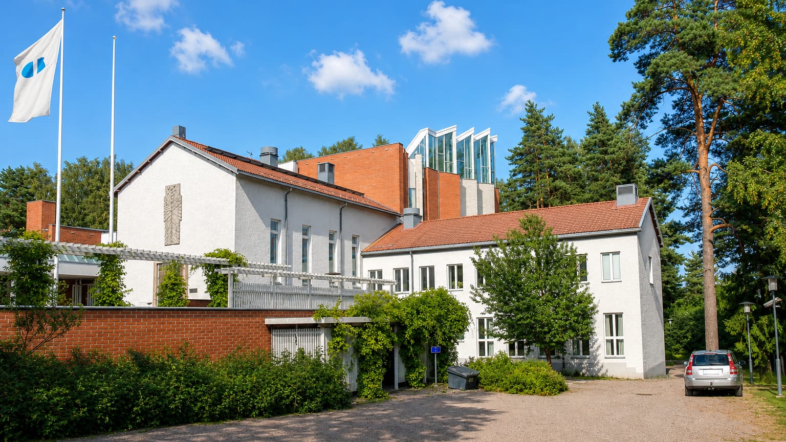 White-rendered and red-brick parish-style building among tall pines in Pakila, Helsinki