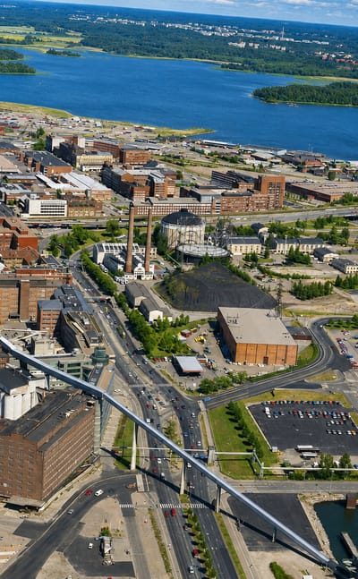Aerial daytime view of Sörnäinen, Helsinki, with red-brick industrial buildings, a pedestrian bridge and a seaside marina on the bay.