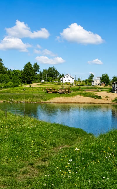 Sunny summer meadow and small pond ringed by grass, trees and scattered houses in Tapaninkylä, Helsinki, Finland.