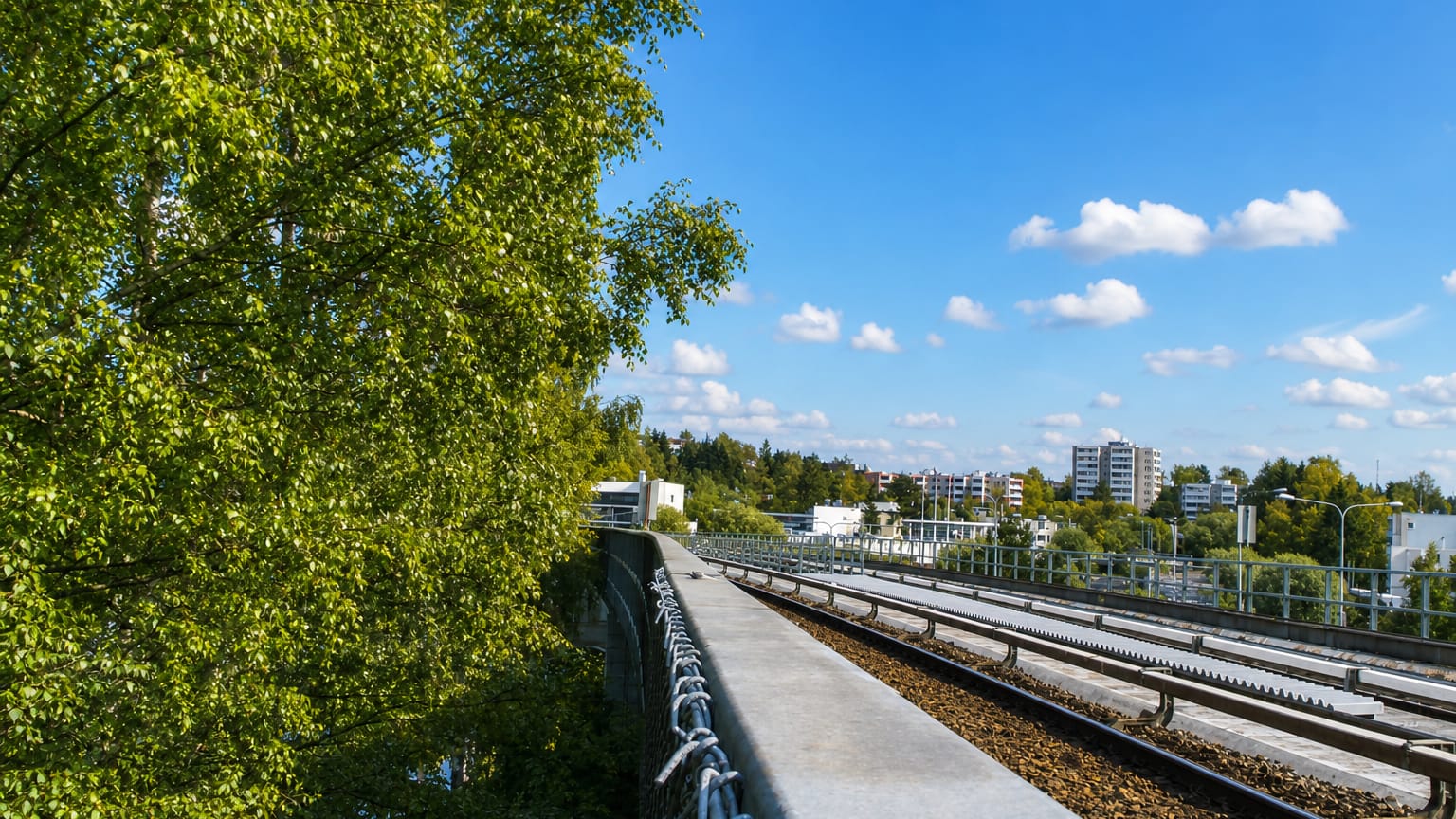 Metro railway on a concrete viaduct beside birch trees and white suburban apartment blocks in Vesala, Helsinki