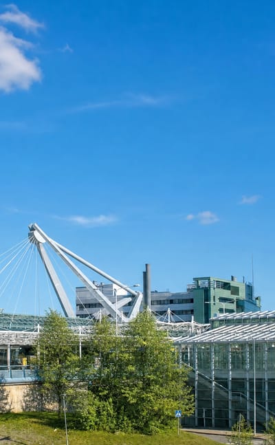 Vuosaari, Helsinki, with its landmark Cirrus high-rise tower above glass-roofed buildings and green spaces under a clear blue sky