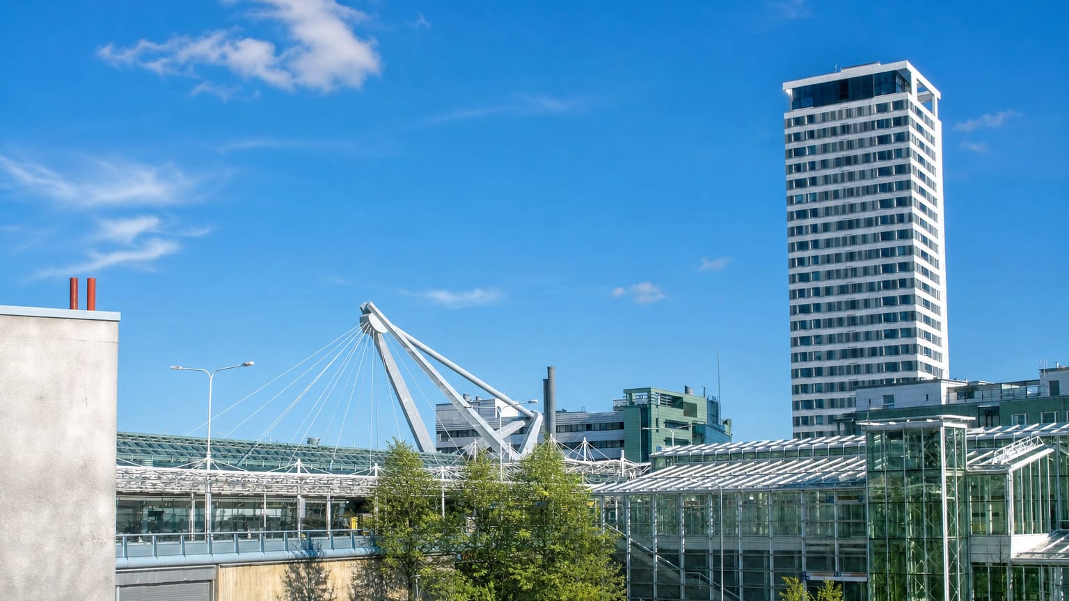 Vuosaari, Helsinki, with its landmark Cirrus high-rise tower above glass-roofed buildings and green spaces under a clear blue sky