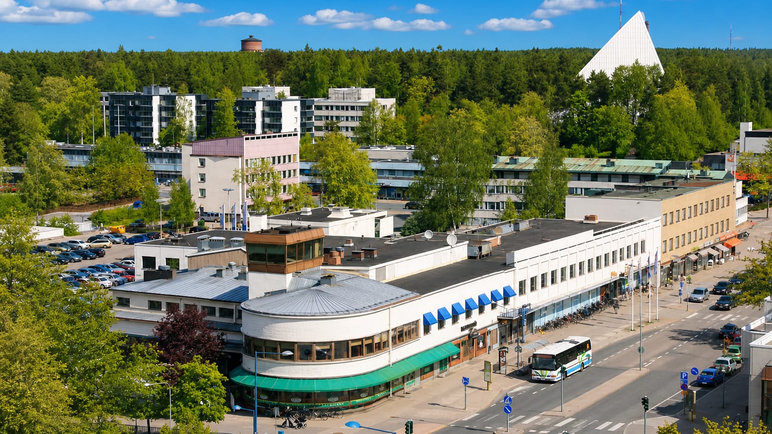 Aerial view of Hyvinge town centre with its triangular white church and water tower above low-rise shops and a local bus.