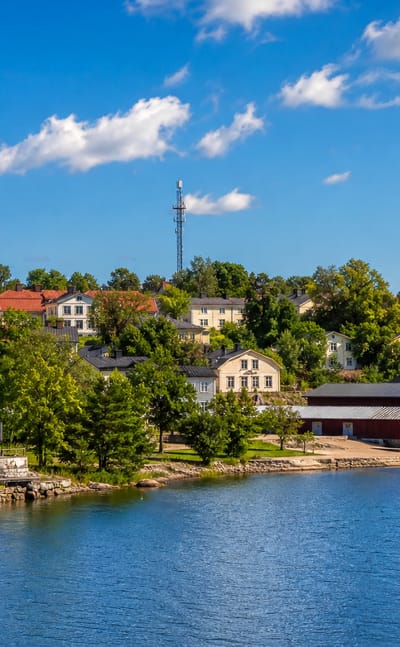 Waterfront view of Pernå village with two church spires, red boathouses and wooden houses among trees, Finland