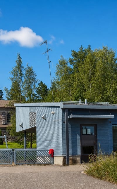 Grey stone church tower behind a modern civic building with a red car parked in Pornainen, Finland.