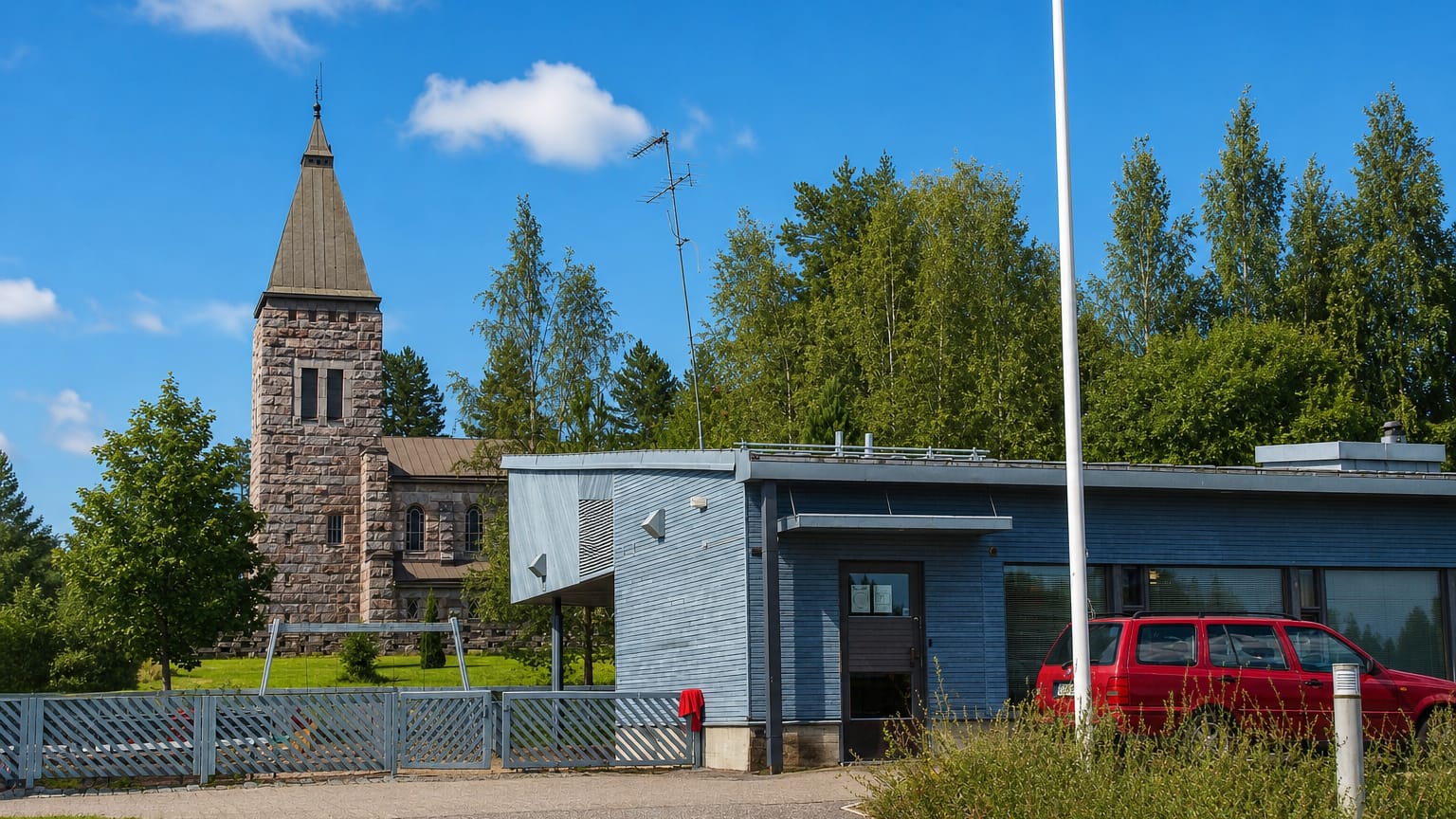 Grey stone church tower behind a modern civic building with a red car parked in Pornainen, Finland.