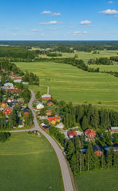 Rural Sibbo village of red wooden houses and a church among green fields and forest in Uusimaa