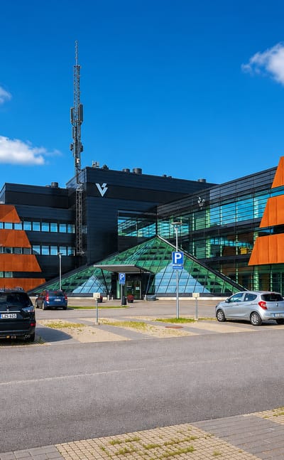Modern glass-and-rust-panel office building with a glass pyramid entrance and parking lot in Koivuhaka, Vantaa.