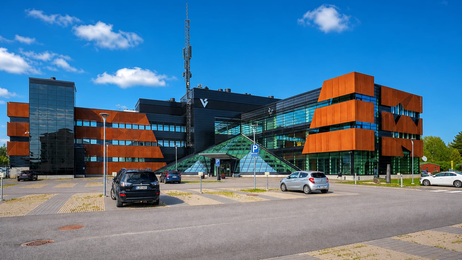 Modern glass-and-rust-panel office building with a glass pyramid entrance and parking lot in Koivuhaka, Vantaa.