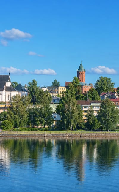 Halikko summer townscape with a white church spire and brick towers reflected in calm river water under a blue sky