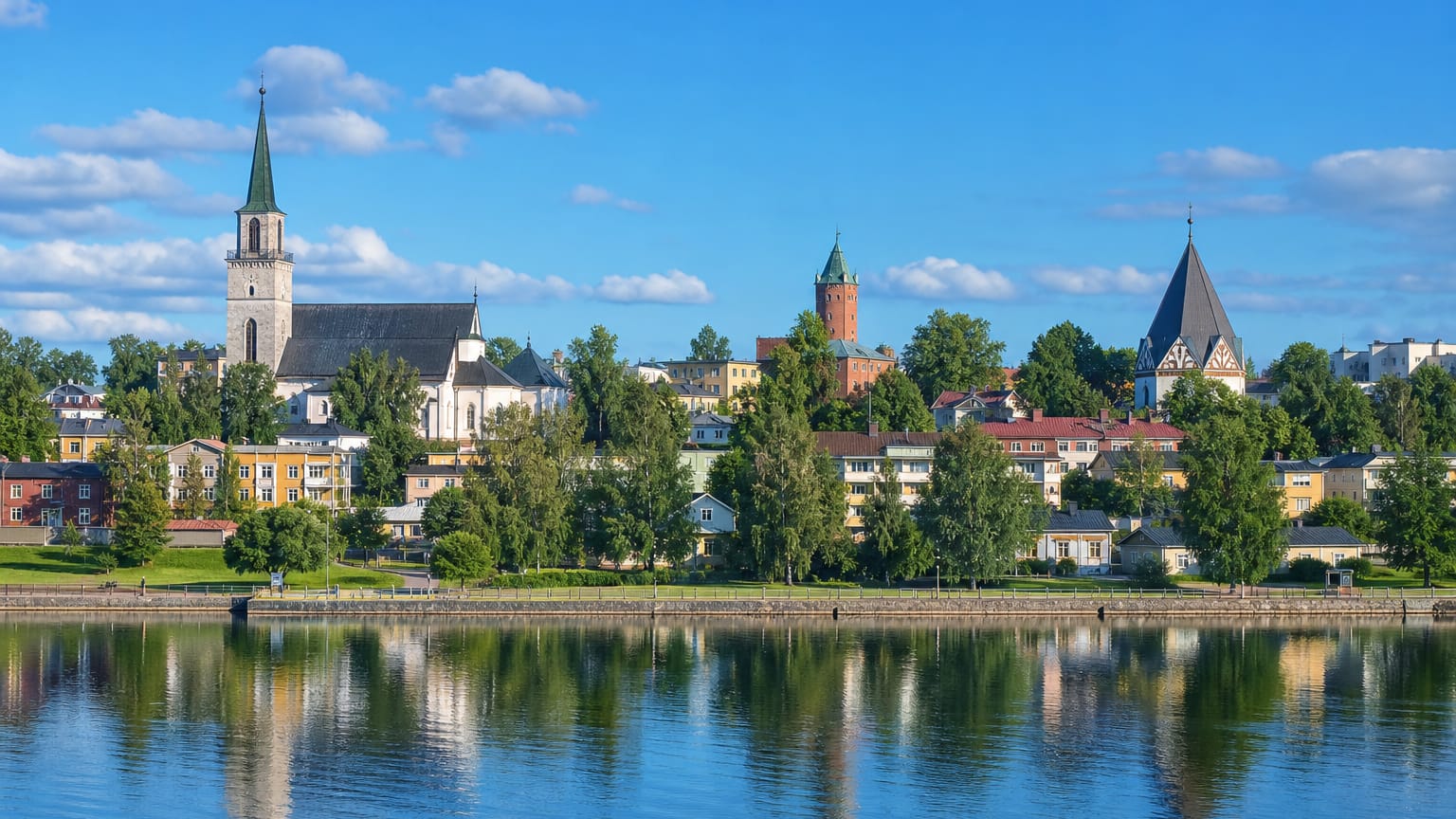 Halikko summer townscape with a white church spire and brick towers reflected in calm river water under a blue sky