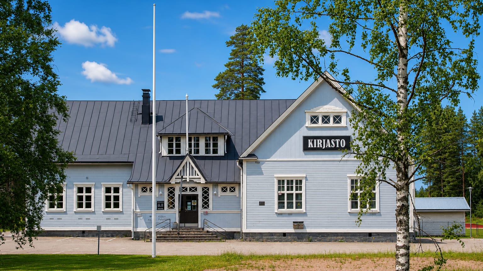 The pale-blue wooden village library, marked Kirjasto, behind birch trees in Kisko, Finland.