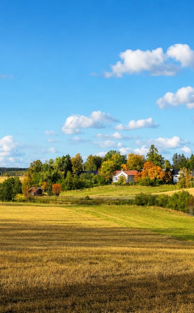 Rolling harvested farm fields, red barns and a farmhouse by a stream in Koski Tl, Finland.