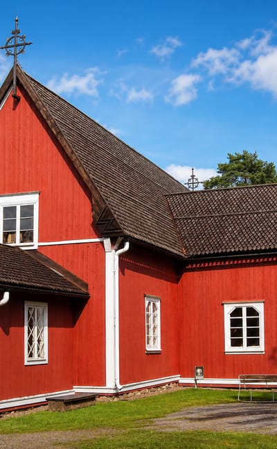 Red wooden church with white trim and an open door on a grassy plot in Kustavi, Finland.