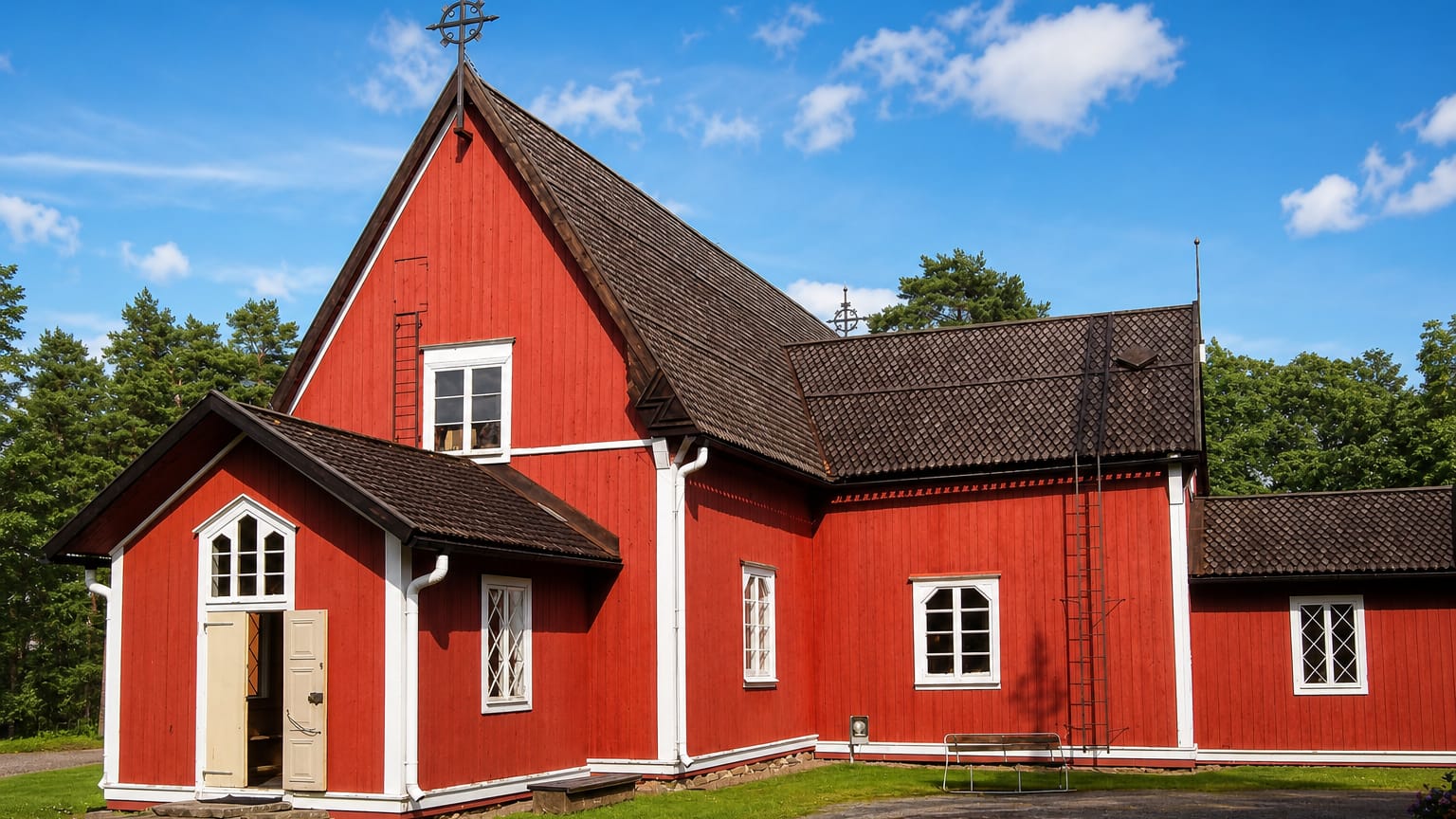 Red wooden church with white trim and an open door on a grassy plot in Kustavi, Finland.