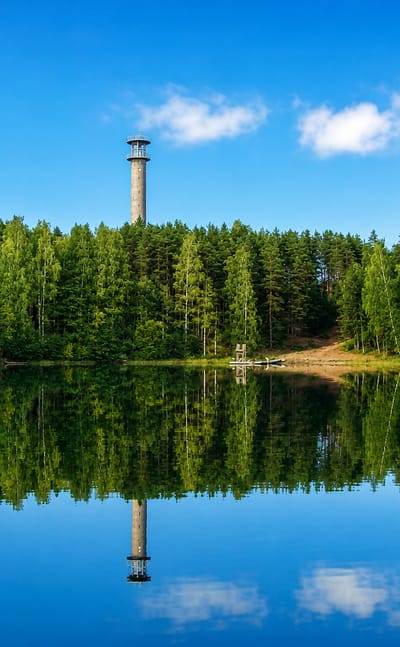 Tall observation tower above spruce-and-birch forest mirrored in a calm lake at Kuusjoki, Finland.