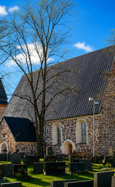 Medieval grey-stone church with a bell tower rising over a graveyard on a bright spring day in Laitila, Finland