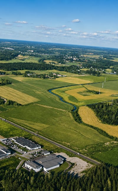 Aerial view over Marttila, Finland, with patchwork farmland, forest, a winding river and roadside buildings under a blue sky.