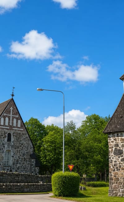 Masku's medieval grey stone church and freestanding bell tower under a blue summer sky in Varsinais-Suomi, Finland