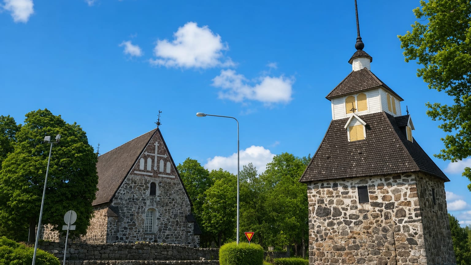 Masku's medieval grey stone church and freestanding bell tower under a blue summer sky in Varsinais-Suomi, Finland