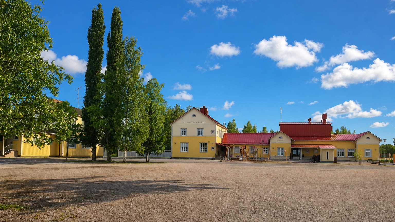 Yellow wooden buildings with red roofs and tall poplars beside a gravel square under a blue sky in Mellilä, Finland.