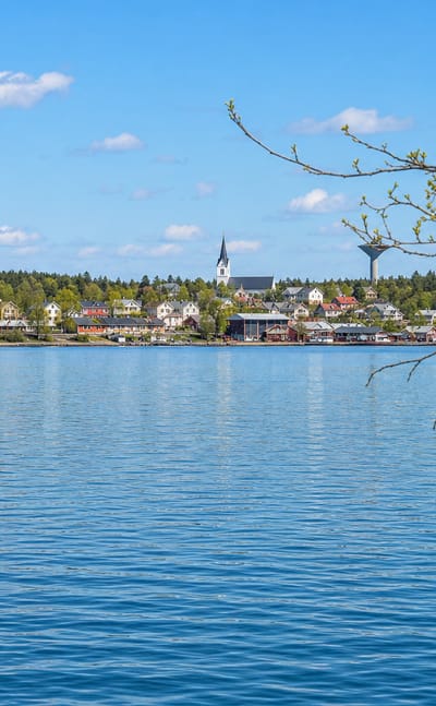 Merimasku townscape across calm blue archipelago water, with a church spire, waterfront houses and spring-green trees