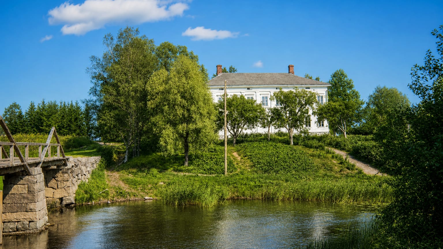White wooden manor on a riverside hill with birches and an old stone footbridge in Mietoinen, Finland