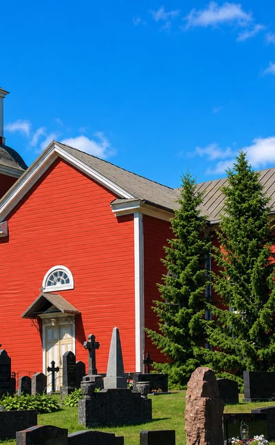 Oripää's red wooden church with a domed bell tower beside an old graveyard under a blue sky.