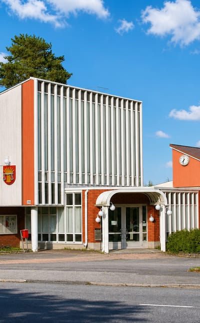 Mid-century civic building with an orange facade and coat-of-arms in Pöytyä, Finland, beside a road.
