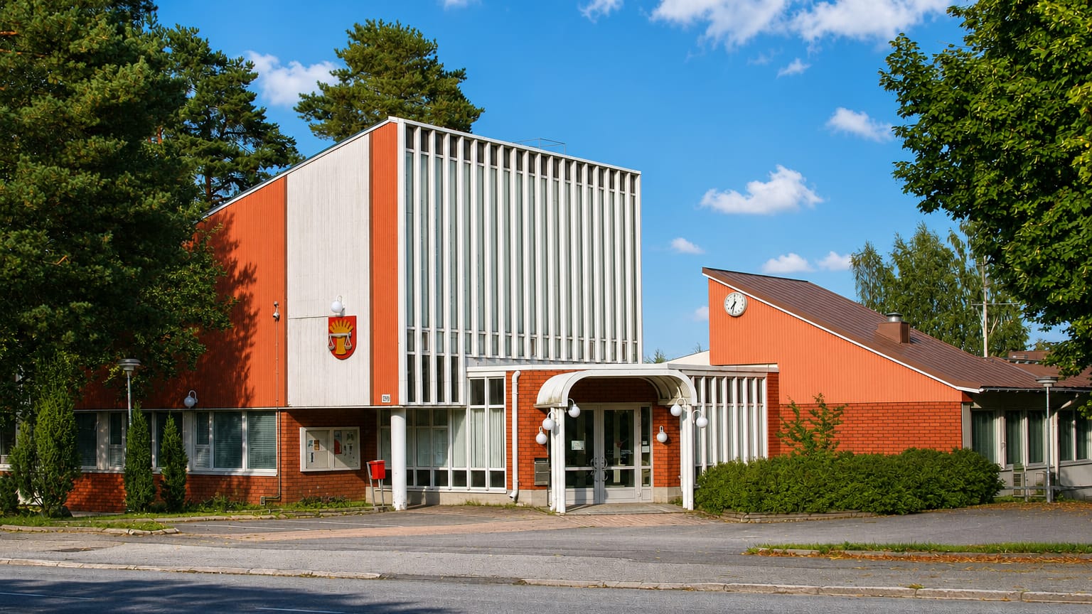 Mid-century civic building with an orange facade and coat-of-arms in Pöytyä, Finland, beside a road.
