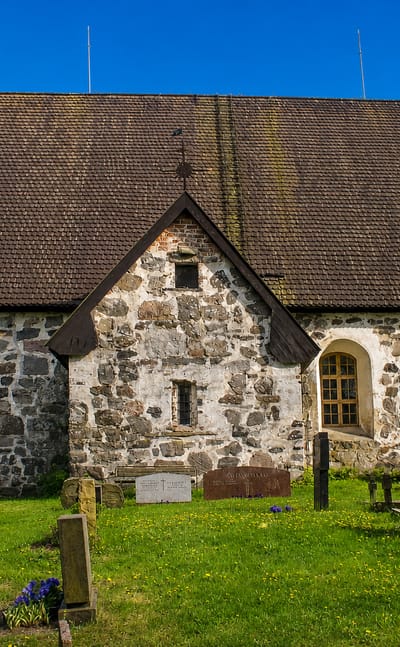 Medieval grey fieldstone church and old graveyard under a blue sky in Rusko, Finland.