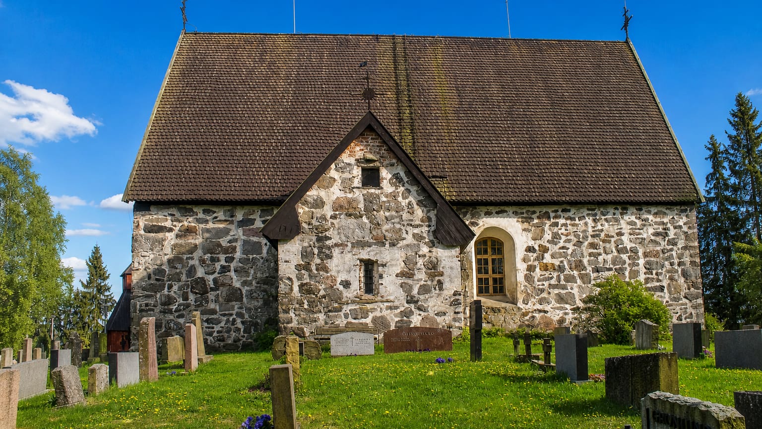 Medieval grey fieldstone church and old graveyard under a blue sky in Rusko, Finland.