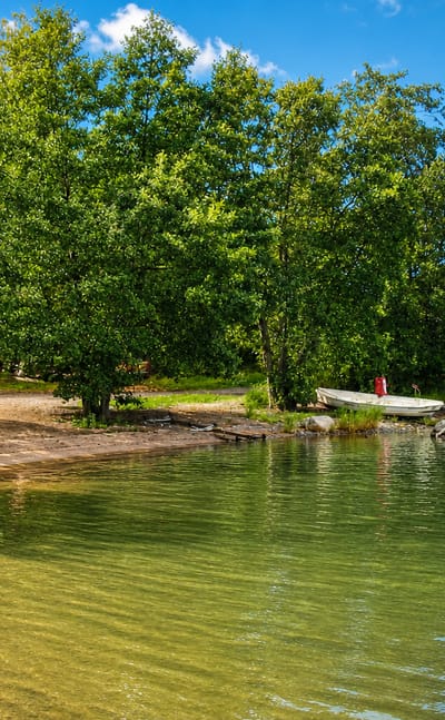 Sandy beach on the archipelago shore at Rymättylä, Finland, with rowboats, birches and a red cottage under a bright summer sky.