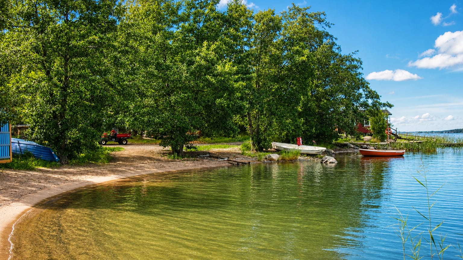 Sandy beach on the archipelago shore at Rymättylä, Finland, with rowboats, birches and a red cottage under a bright summer sky.