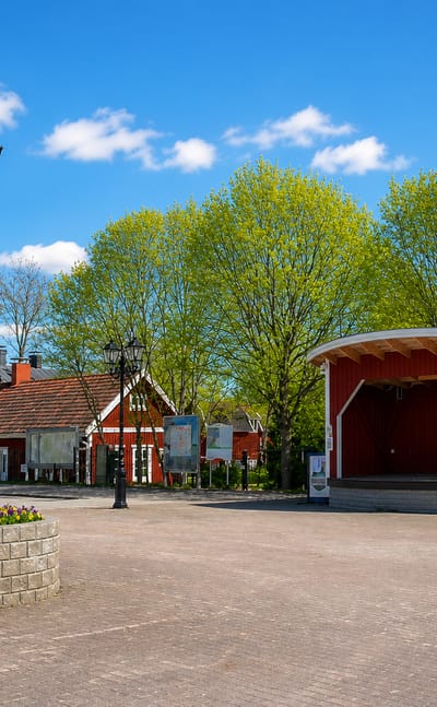 Village square in Sauvo, Finland, with a red bandstand, ornate lamp post and flower bed under a blue sky