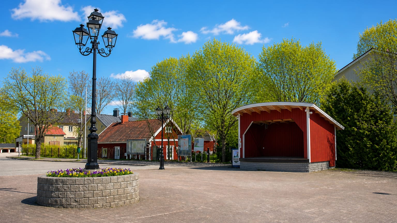 Village square in Sauvo, Finland, with a red bandstand, ornate lamp post and flower bed under a blue sky