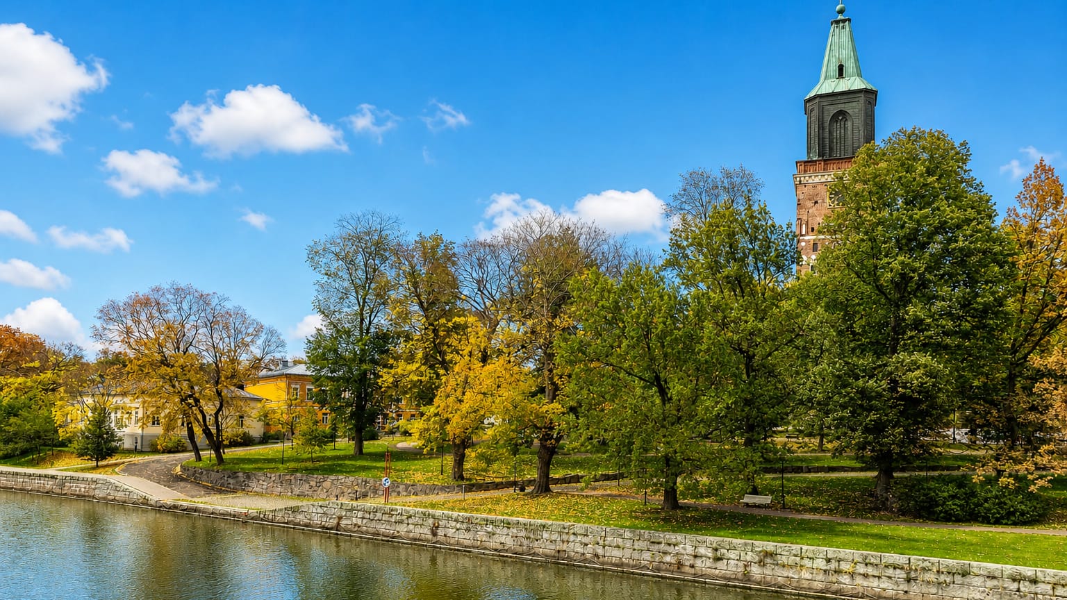 Turku Cathedral's green-spired tower above autumn trees along the Aura River in Turku, Finland