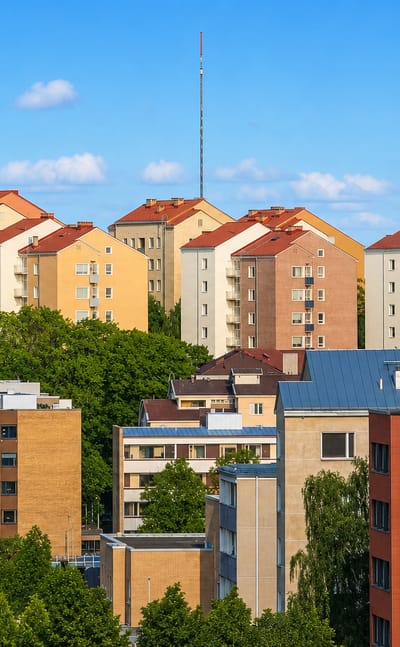 Pastel post-war apartment blocks with red roofs in III kaupunginosa, Turku, seen above the treetops.