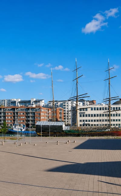 Turku's Itäranta waterfront with a moored tall ship, brick apartment blocks and a wide riverside plaza.
