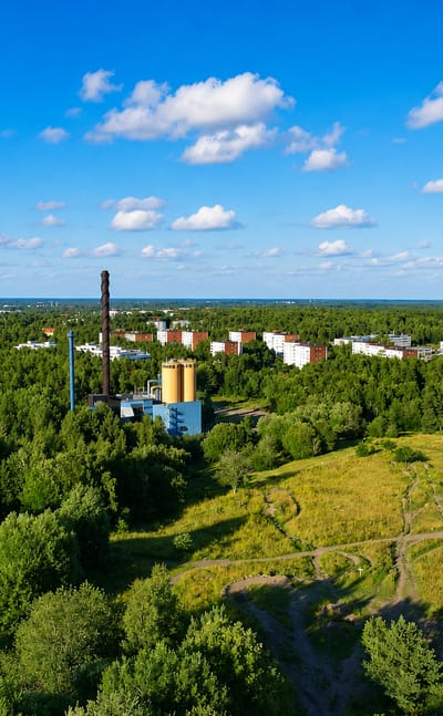 Aerial view of forest, meadow paths and a heating-plant chimney beside apartment blocks in Luolavuori, Turku.
