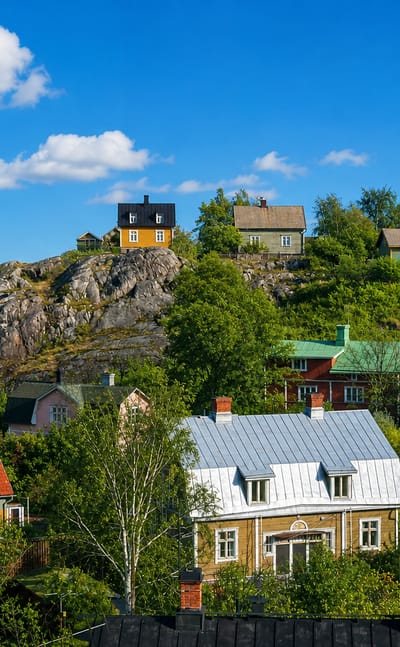 Traditional painted wooden houses on a rocky hill above apartment blocks and birch trees in Nummi, Turku, Finland