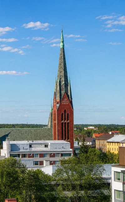 Red-brick neo-Gothic church spire rising above apartment blocks and leafy streets in the Port Arthur district of Turku, Finland.