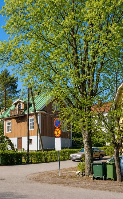 Street corner in Puistomäki, Turku, lined with yellow and brown wooden houses under fresh spring foliage.